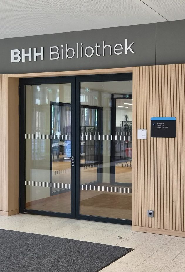 Moderner Bürogebäudekomplex mit großen Fenstern und Baustellenkränen im Hintergrund.